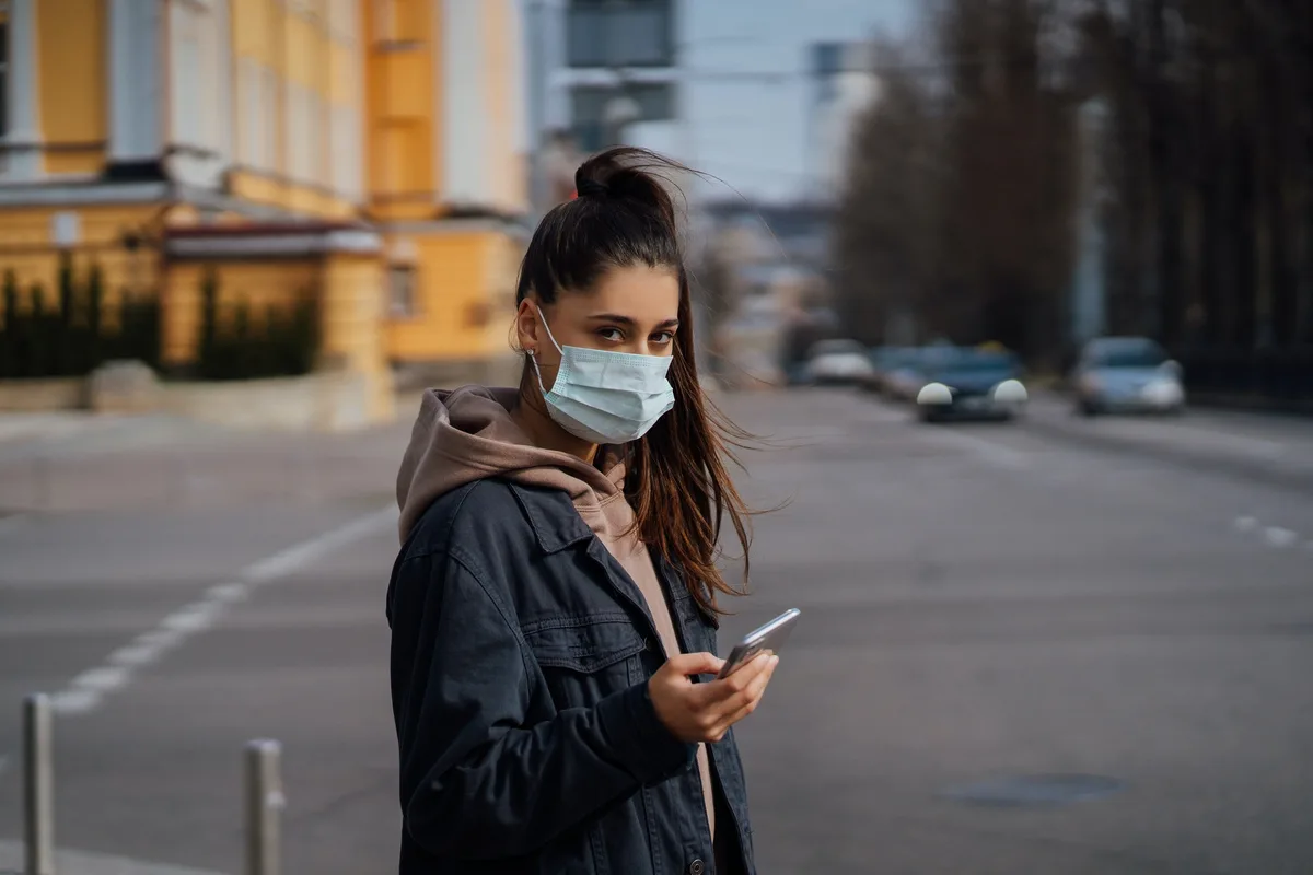Girl in protective mask using smartphone outdoors. COVID 19. World coronavirus pandemic