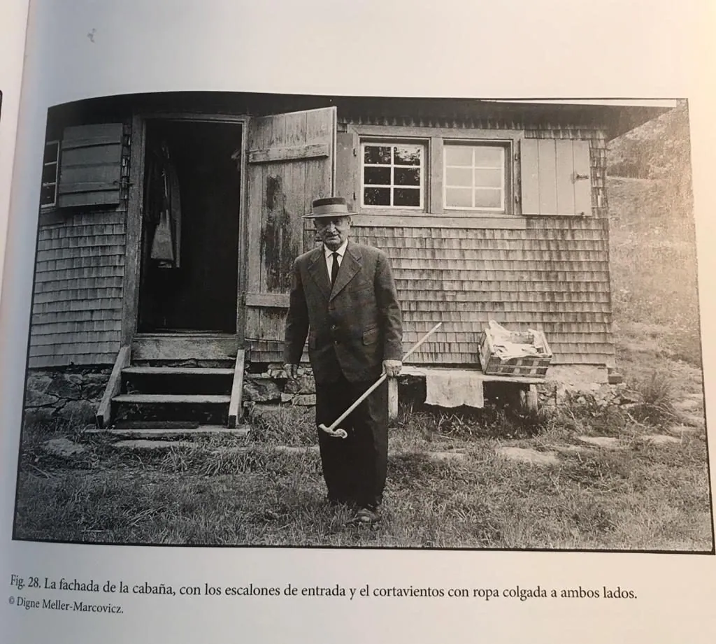 Reproducción de una fotografía de Heidegger ante la puerta de una cabaña de madera.