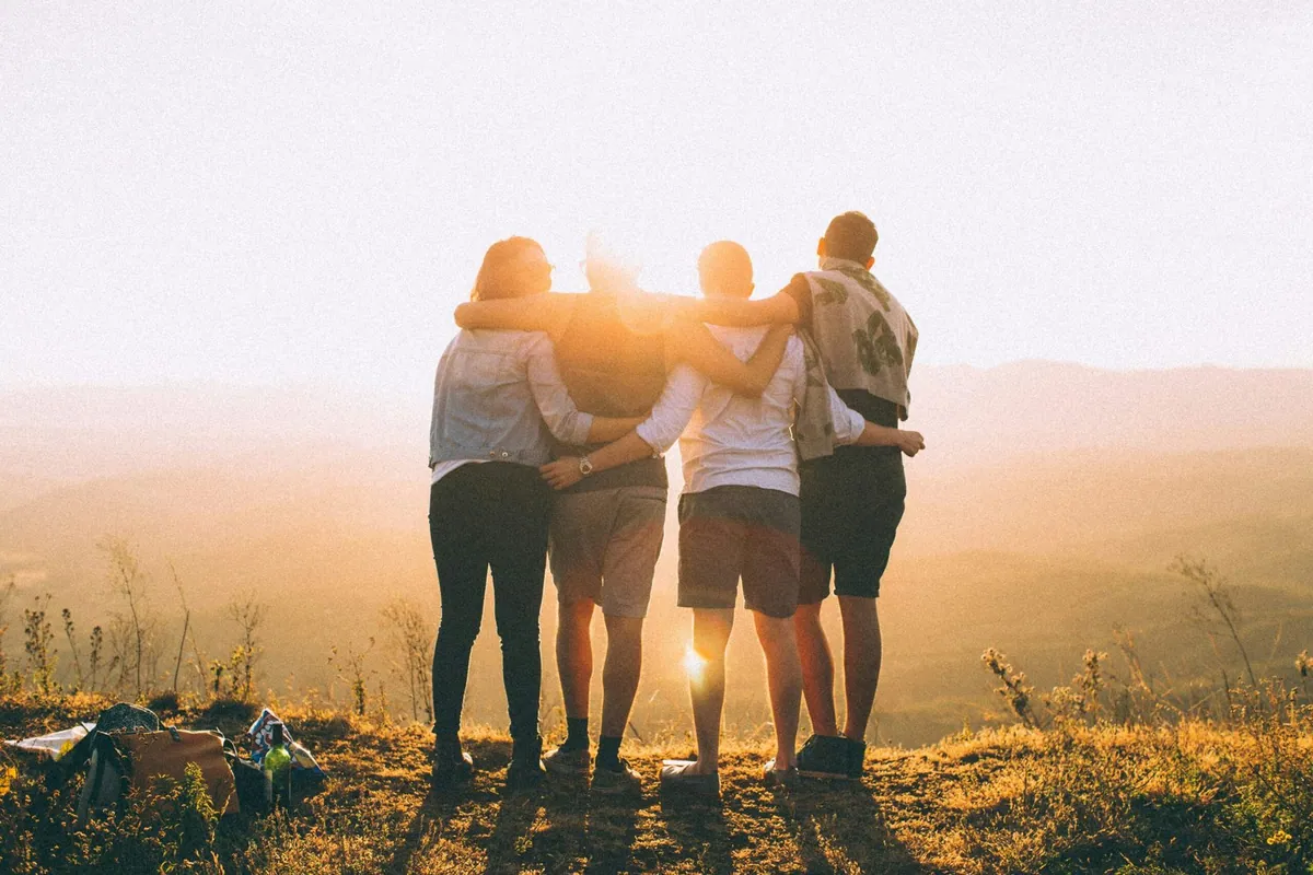 Cuatro personas se abrazan de espaldas frente a un paisaje al atardecer.