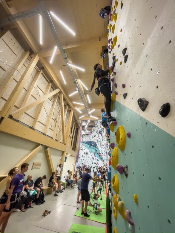 Persona escalando en un muro interior ante otras personas