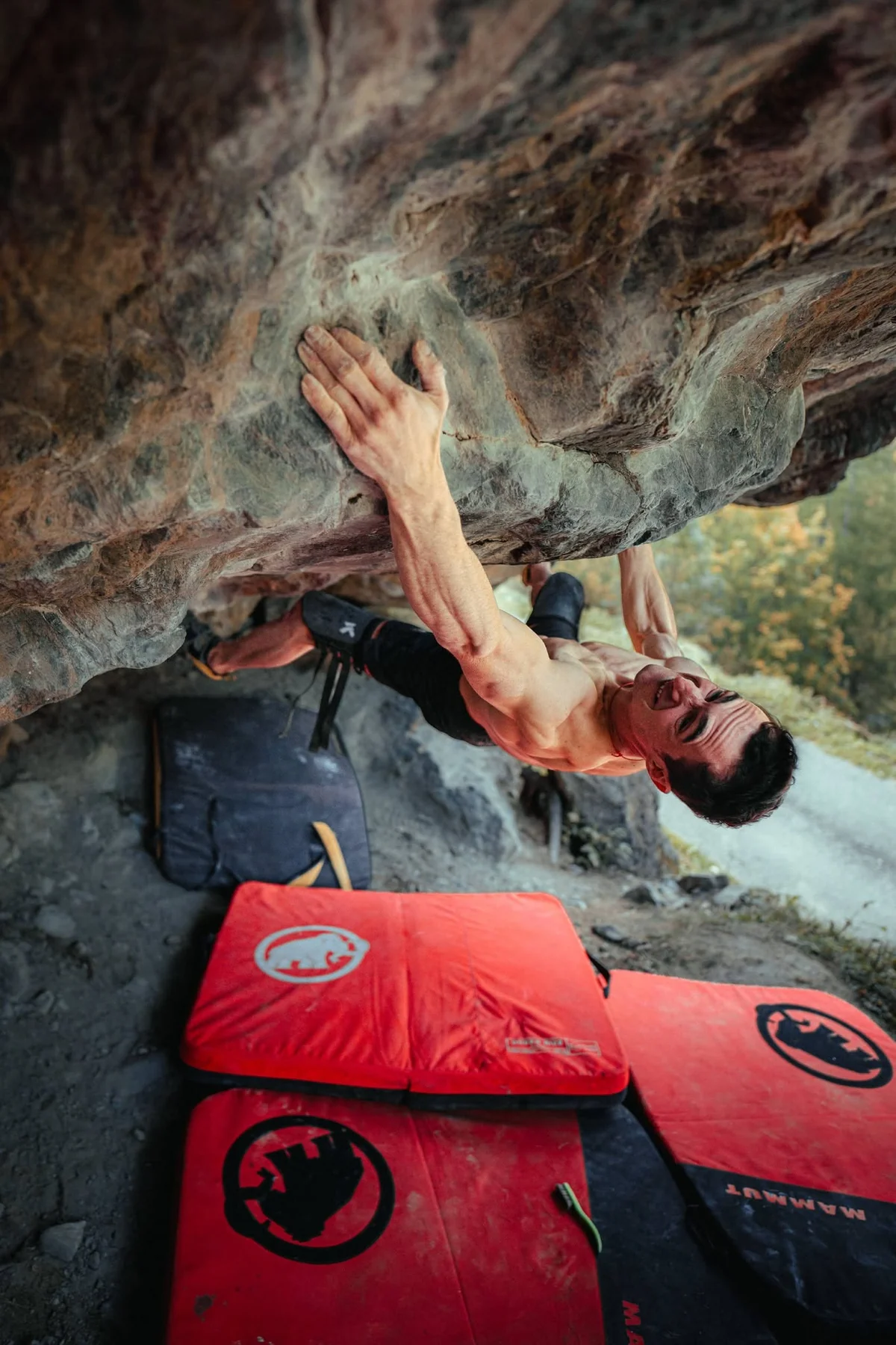 Adam Ondra escalando bajo el techo de Exodia, con colchonetas de bloque sobre el suelo.