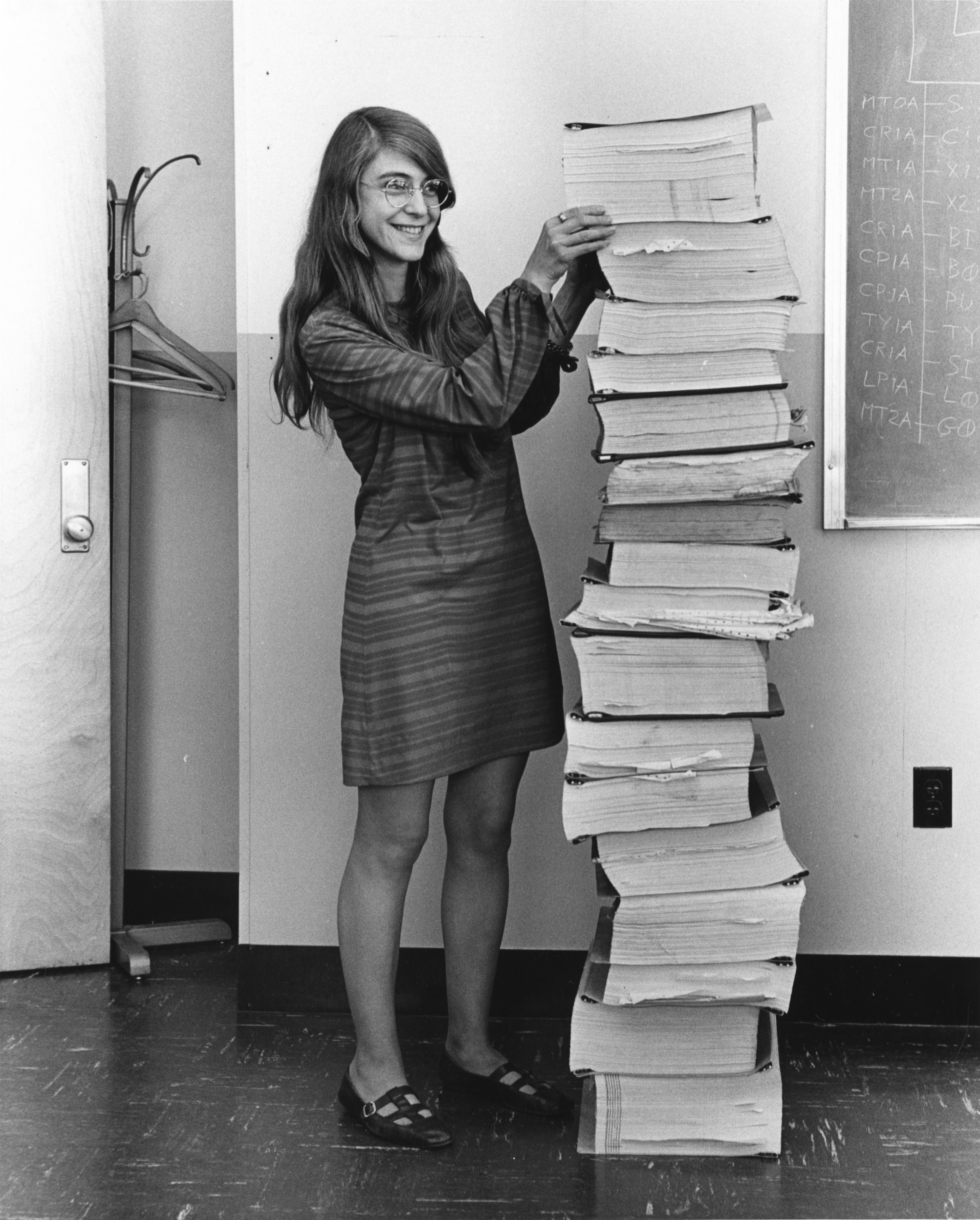 Margaret Hamilton de pie junto a una torre de listados impresos del software de vuelo del programa Apolo, desarrollado por ella y su equipo.