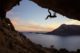 Male climber climbing along roof in cave against beautiful view of coast below
